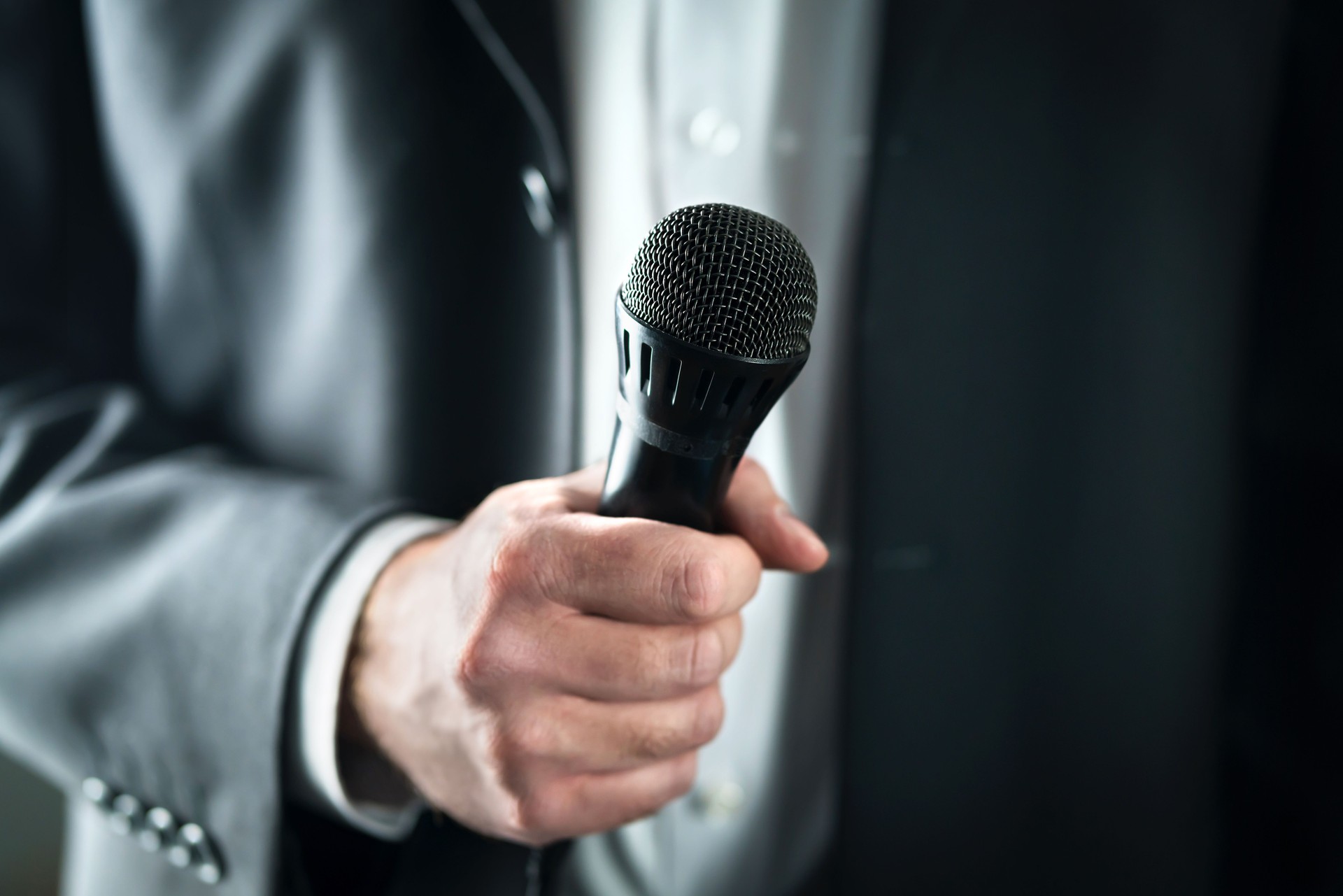 Business man holding microphone. Public speaking and giving speech in suit for audience concept. Fiance, host or best man giving toast with mic in wedding.